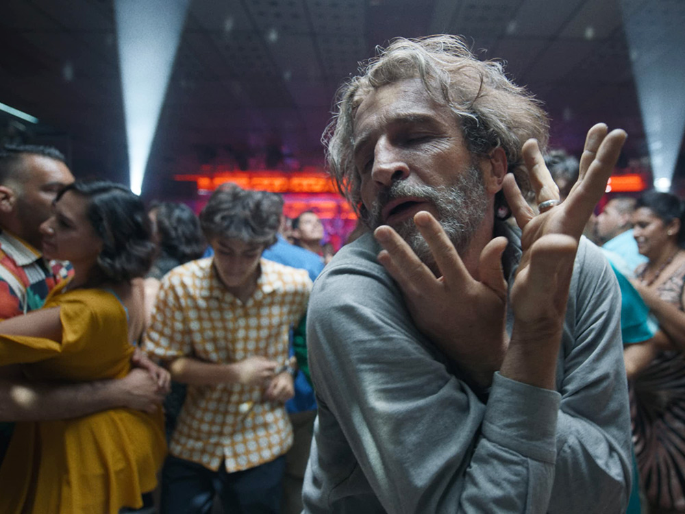 An older man dances passionately against a crowd of couples