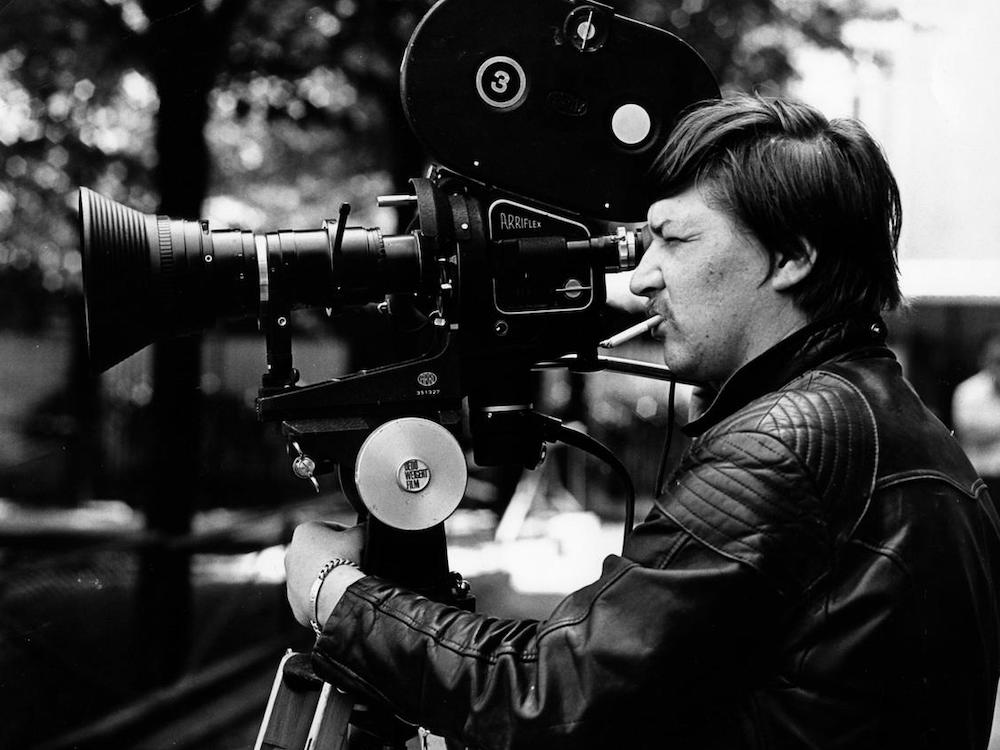 A side shot of Rainer Werner Fassbender looking into a camera, cigarette hanging from his mouth